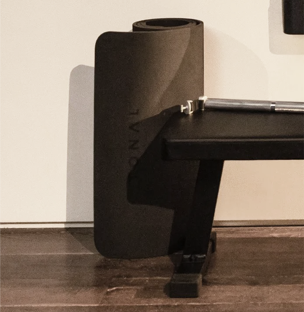 Close up of the Tonal exercise mat, flat bench, and bar attachment set against a wall