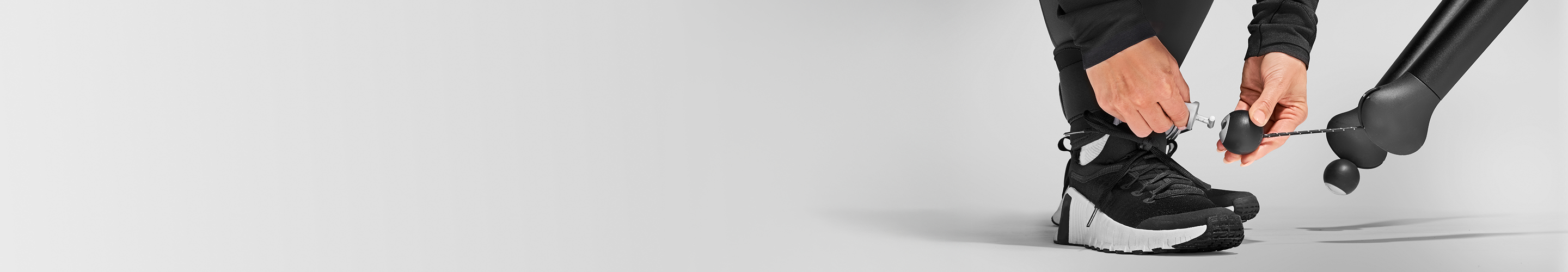 Person clipping Tonal ankle straps to cable on a grey background.