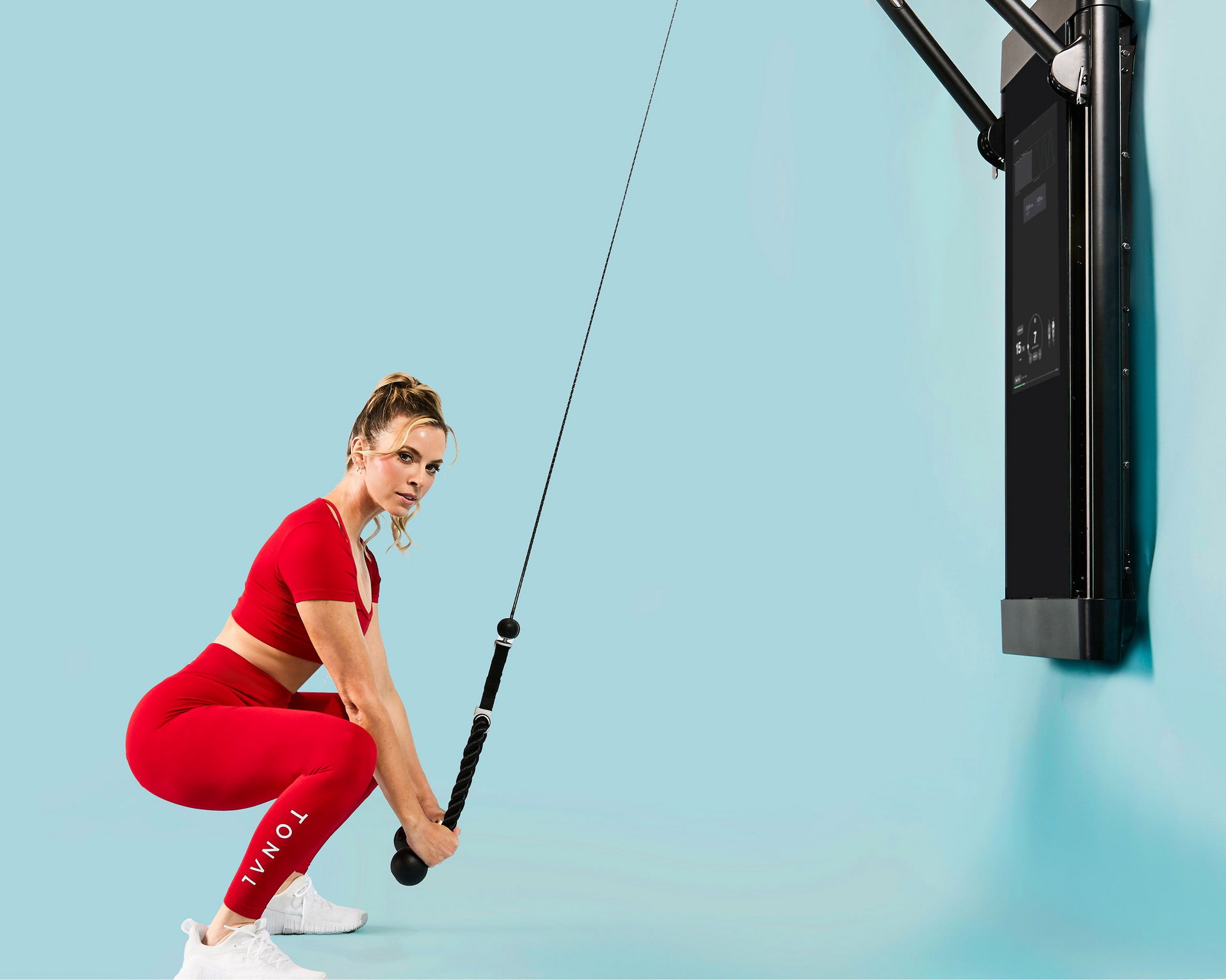 Women in red athletic outfit doing a HIIT workout using rope attachment and Tonal machine